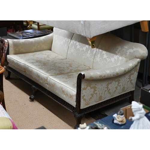 491 - A carved mahogany wing-armed sofa, in old gold damask upholstery, three ball and claw front supports... 