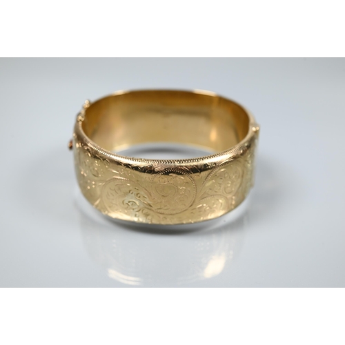 216 - A 9ct yellow gold oval half-hinged wide bangle with chased foliate decoration (missing safety chain)... 