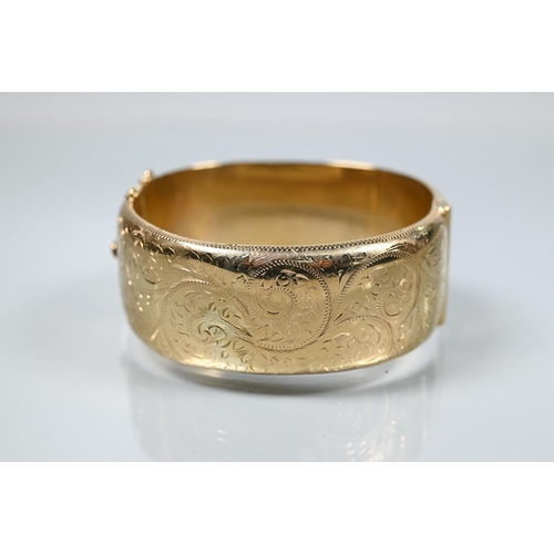 216 - A 9ct yellow gold oval half-hinged wide bangle with chased foliate decoration (missing safety chain)... 