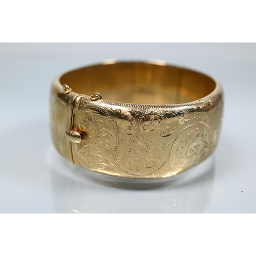 216 - A 9ct yellow gold oval half-hinged wide bangle with chased foliate decoration (missing safety chain)... 