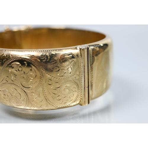 216 - A 9ct yellow gold oval half-hinged wide bangle with chased foliate decoration (missing safety chain)... 