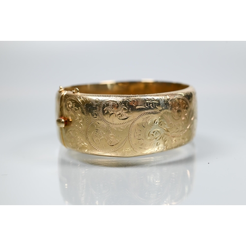 216 - A 9ct yellow gold oval half-hinged wide bangle with chased foliate decoration (missing safety chain)... 