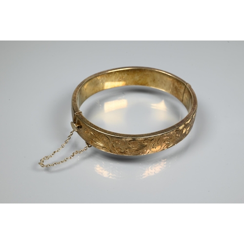 225 - A silver-gilt half-hinged oval bangle with foliate engraved decoration, and safety chain attached, a... 