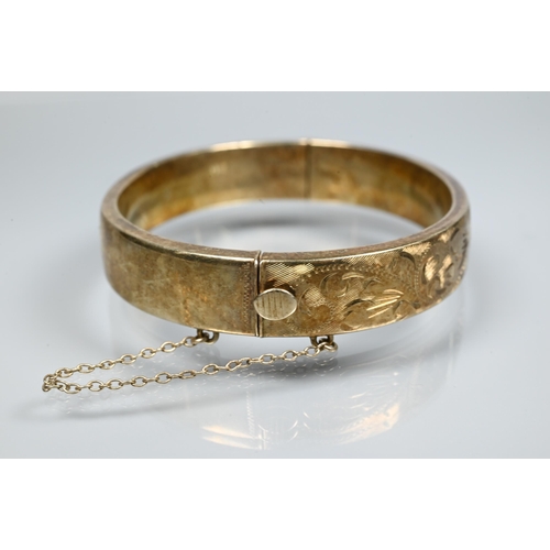 225 - A silver-gilt half-hinged oval bangle with foliate engraved decoration, and safety chain attached, a... 