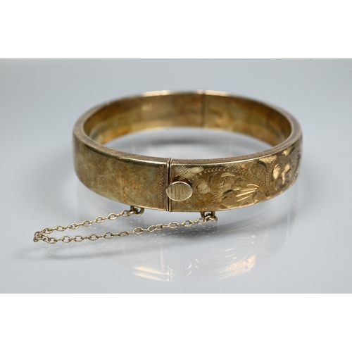 225 - A silver-gilt half-hinged oval bangle with foliate engraved decoration, and safety chain attached, a... 