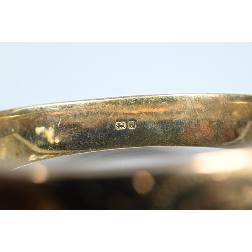 225 - A silver-gilt half-hinged oval bangle with foliate engraved decoration, and safety chain attached, a... 