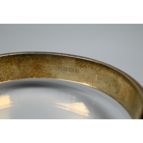 225 - A silver-gilt half-hinged oval bangle with foliate engraved decoration, and safety chain attached, a... 