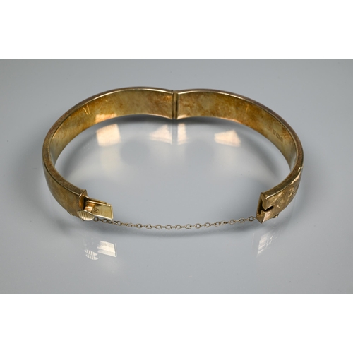 225 - A silver-gilt half-hinged oval bangle with foliate engraved decoration, and safety chain attached, a... 