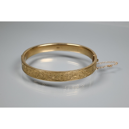 227 - A 9ct yellow gold oval half-hinged bangle with foliate decoration, concealed clasp and safety chain ... 