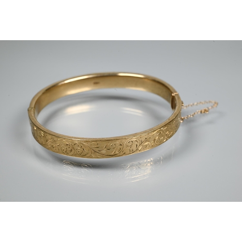 227 - A 9ct yellow gold oval half-hinged bangle with foliate decoration, concealed clasp and safety chain ... 