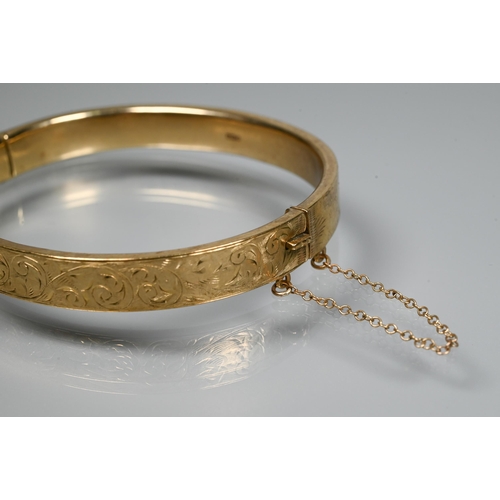 227 - A 9ct yellow gold oval half-hinged bangle with foliate decoration, concealed clasp and safety chain ... 