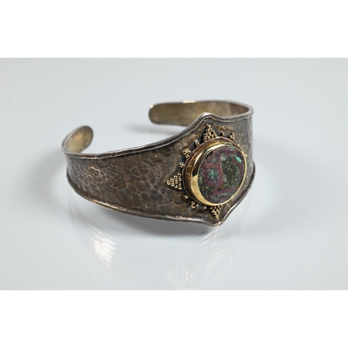 344 - An Arts & Crafts style bangle with hammered finish and central mounted stone boss with beadwork ... 