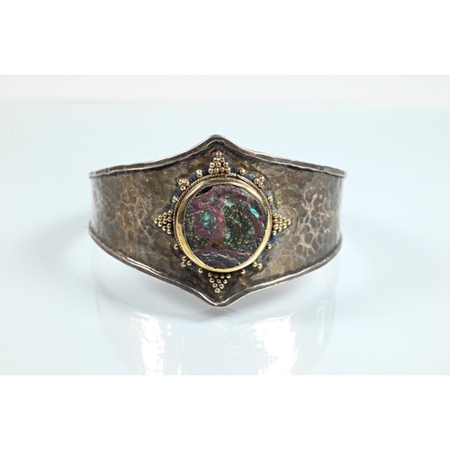 344 - An Arts & Crafts style bangle with hammered finish and central mounted stone boss with beadwork ... 