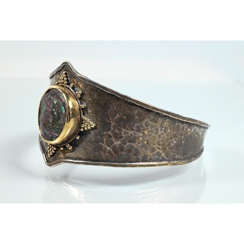 344 - An Arts & Crafts style bangle with hammered finish and central mounted stone boss with beadwork ... 