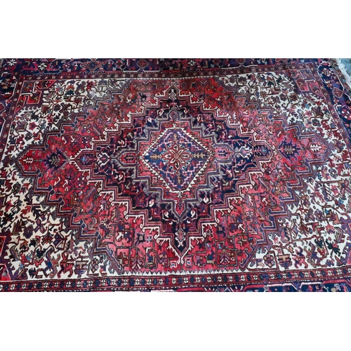 801 - A Persian Heriz carpet of traditional design, the red ground centred by a medallion in reds and blue... 