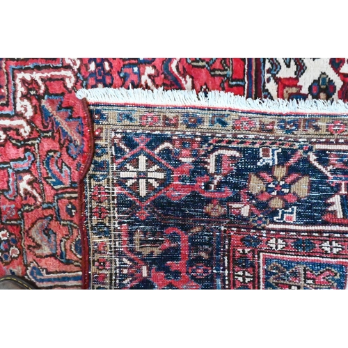 801 - A Persian Heriz carpet of traditional design, the red ground centred by a medallion in reds and blue... 