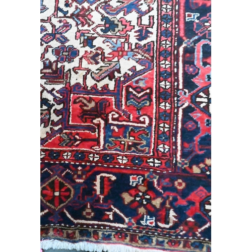 801 - A Persian Heriz carpet of traditional design, the red ground centred by a medallion in reds and blue... 