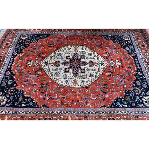 802 - A hand-made Persian Heriz carpet, centred by a camel ground oval tablet on salmon-red ground, 347 cm... 