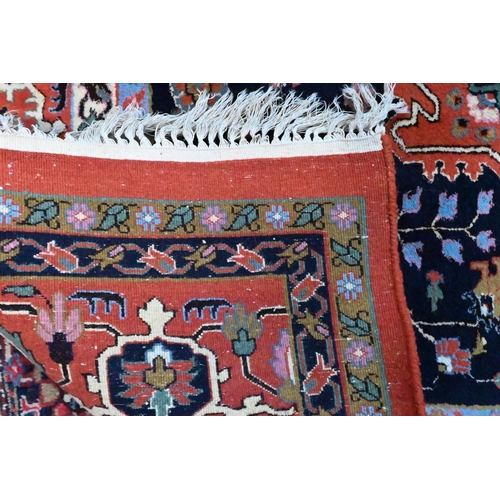 802 - A hand-made Persian Heriz carpet, centred by a camel ground oval tablet on salmon-red ground, 347 cm... 