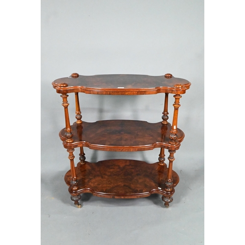 865 - A Victorian figured walnut three-tier whatnot, of all-round serpentine form, raised on brass castors... 