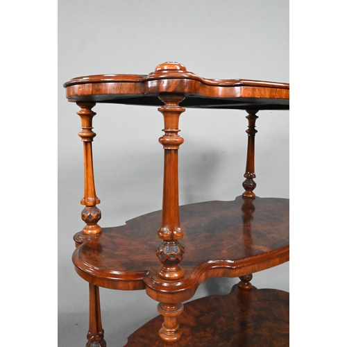 865 - A Victorian figured walnut three-tier whatnot, of all-round serpentine form, raised on brass castors... 