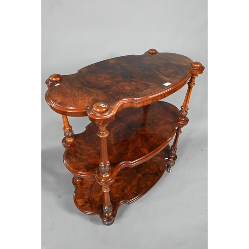 865 - A Victorian figured walnut three-tier whatnot, of all-round serpentine form, raised on brass castors... 