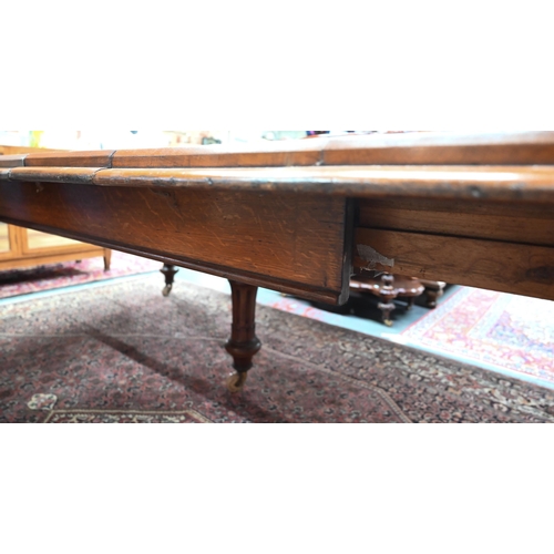 869 - A large Victorian golden oak extending table, the wind action top with rounded corners accepting the... 