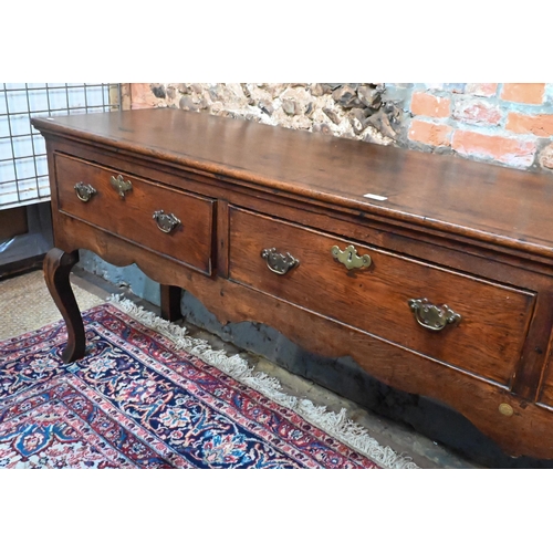 914 - An 18th century cross-banded oak low dresser, with three cock-beaded frieze drawers over a wavy apro... 