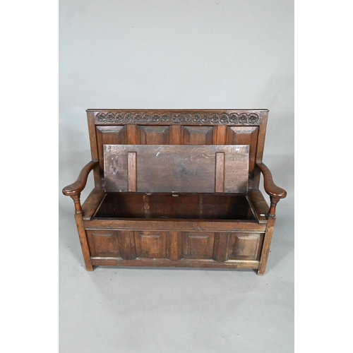 925 - An antique oak box settle, the panelled back with floral carved rosette's over shaped arms and an ir... 