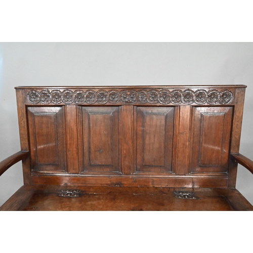 925 - An antique oak box settle, the panelled back with floral carved rosette's over shaped arms and an ir... 