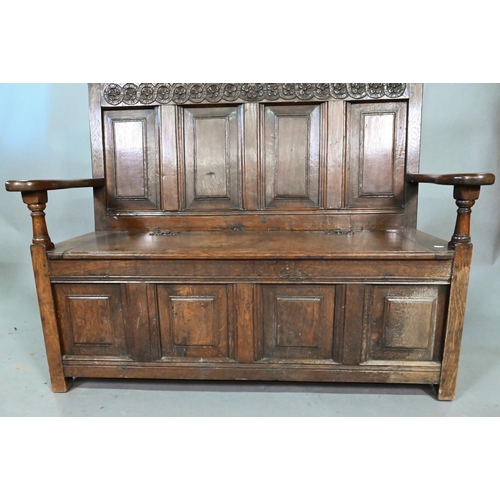 925 - An antique oak box settle, the panelled back with floral carved rosette's over shaped arms and an ir... 