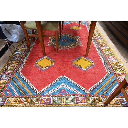 547 - A Moroccan carpet, geometric design on red ground repeating colourful borders, 240 x 160 cm