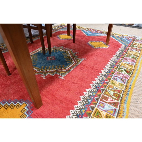 547 - A Moroccan carpet, geometric design on red ground repeating colourful borders, 240 x 160 cm