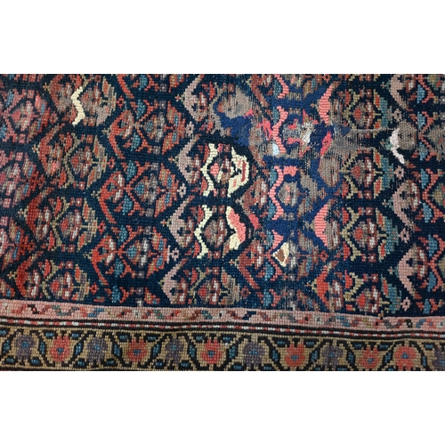 563 - A worn antique Kurdish rug, repeating stylised floral motif on dark blue ground, rosette borders, a/... 