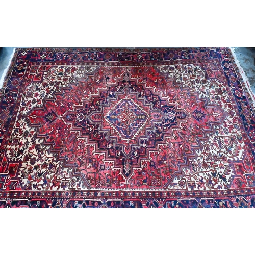 1062 - A Persian Heriz carpet of traditional design, the red ground centred by a medallion in reds and blue... 