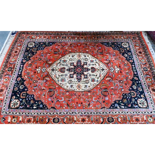 1077 - A hand-made Persian Heriz carpet, centred by a camel ground oval tablet on salmon-red ground, 347 cm... 