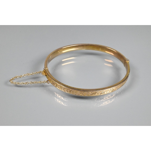 354 - A 9ct yellow gold half hinged oval bangle, with engraved scroll decoration to one side, safety chain... 