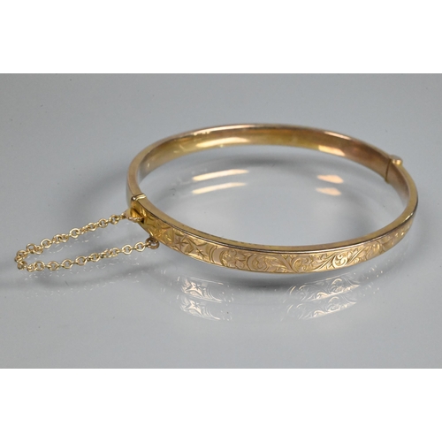 354 - A 9ct yellow gold half hinged oval bangle, with engraved scroll decoration to one side, safety chain... 