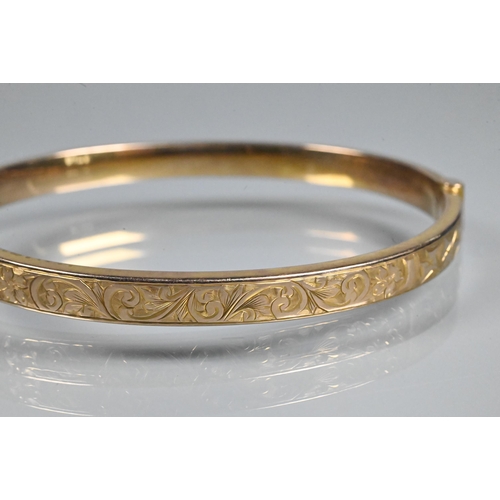 354 - A 9ct yellow gold half hinged oval bangle, with engraved scroll decoration to one side, safety chain... 