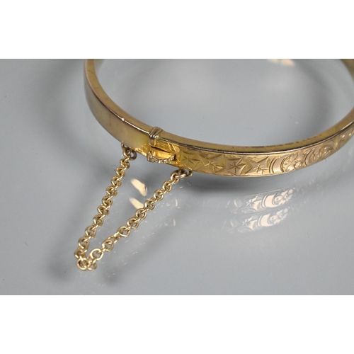 354 - A 9ct yellow gold half hinged oval bangle, with engraved scroll decoration to one side, safety chain... 