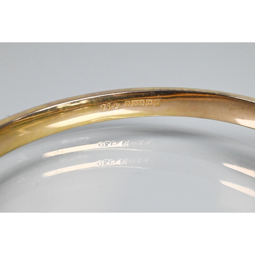 354 - A 9ct yellow gold half hinged oval bangle, with engraved scroll decoration to one side, safety chain... 