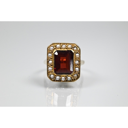 356 - A yellow metal ring of rectangular design featuring emerald-cut red stone, probably garnet, surround... 