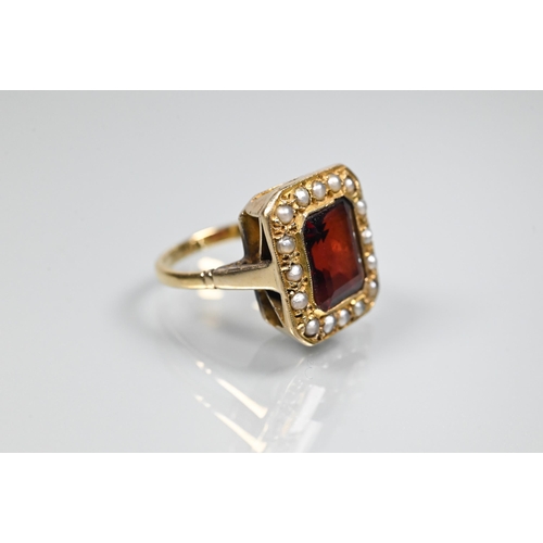 356 - A yellow metal ring of rectangular design featuring emerald-cut red stone, probably garnet, surround... 