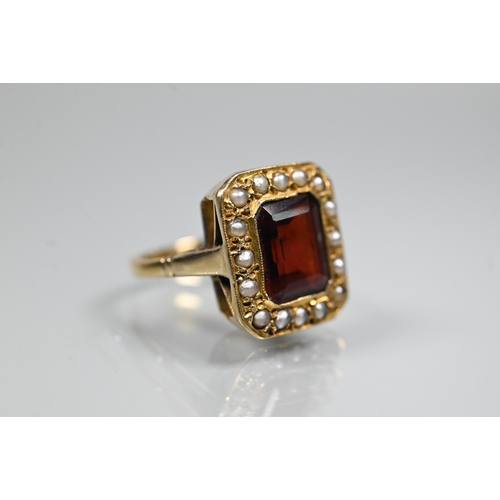 356 - A yellow metal ring of rectangular design featuring emerald-cut red stone, probably garnet, surround... 