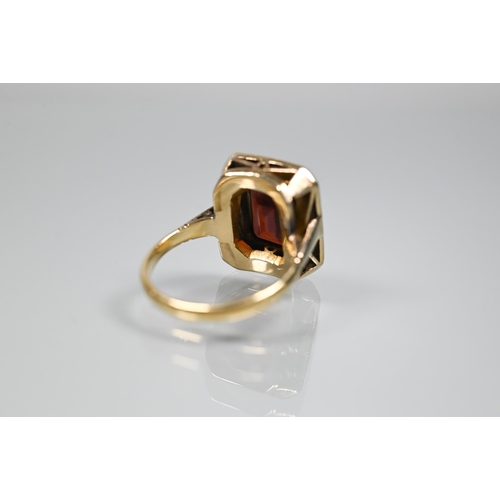 356 - A yellow metal ring of rectangular design featuring emerald-cut red stone, probably garnet, surround... 