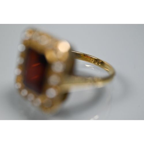 356 - A yellow metal ring of rectangular design featuring emerald-cut red stone, probably garnet, surround... 