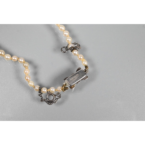 358 - A graduated row of cultured pearls double knotted throughout onto white metal snap in the form of a ... 