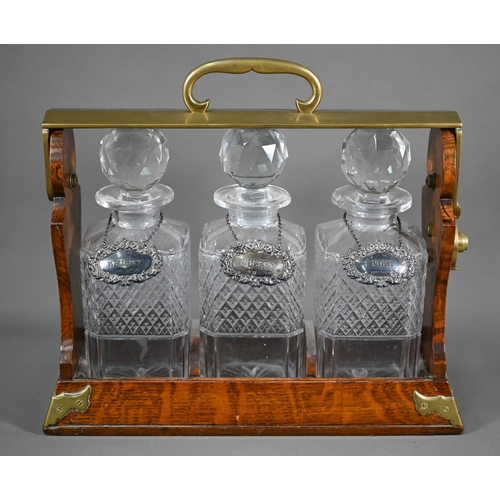 1025 - The Tantalus, an antique Betjemanns Patent brass mounted oak three bottle tantalus, with silver bott... 