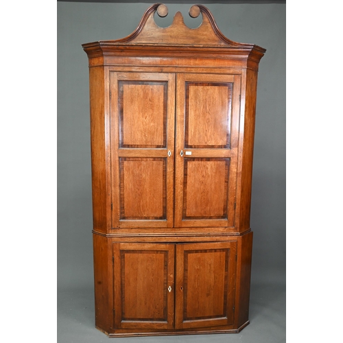 1028 - A Georgian oak corner cupboard, in two parts, the upper with broken swan-neck pediment over a pair o... 