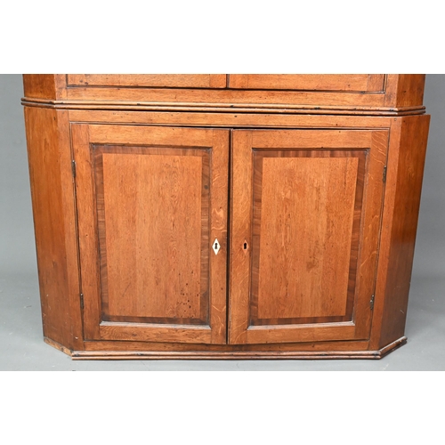 1028 - A Georgian oak corner cupboard, in two parts, the upper with broken swan-neck pediment over a pair o... 